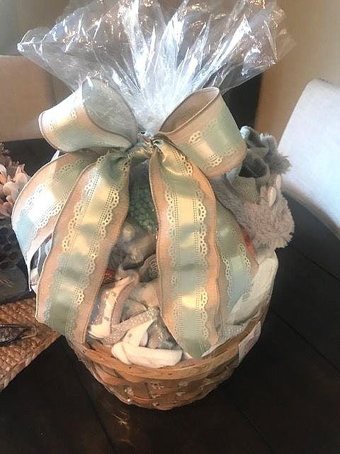Baby shower basket with baby clothes and booties under a sage green ribbon bow