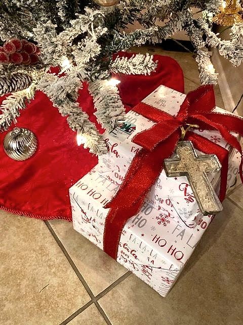 Christmas presents in red-and-white paper with red ribbon and a wooden cross ornament under the tree