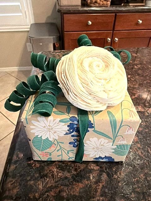 Gift in floral paper topped with a cream paper rose and green curly ribbon