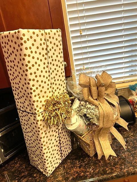 Tall gift in gold polka-dot paper with a gold bow, next to a basket with a burlap bow