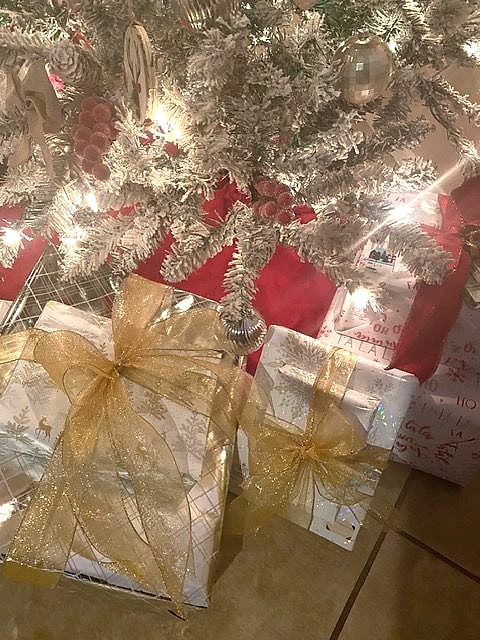 Presents wrapped in silver paper with sheer gold ribbon under a white Christmas tree