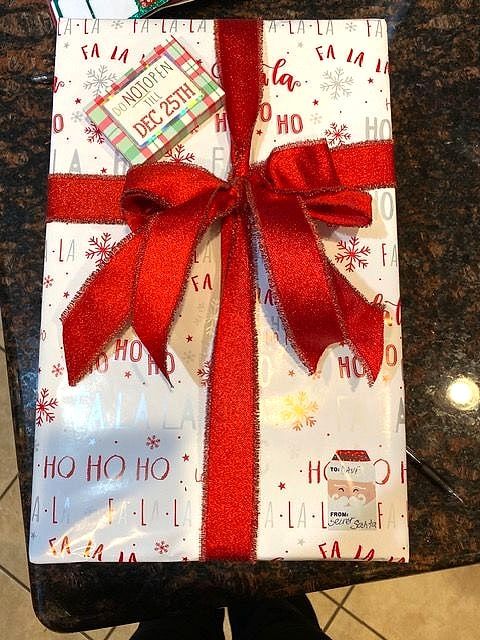 Present wrapped in 'Ho Ho Ho' paper with a sparkly red ribbon and gift tag